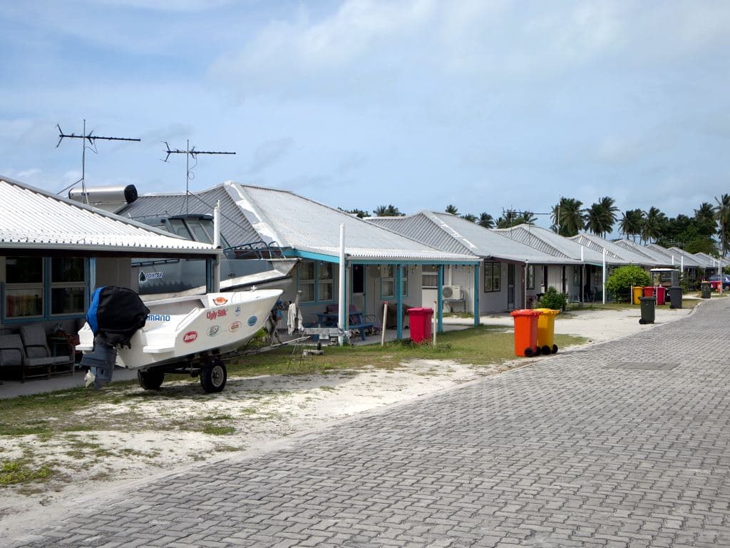 Cocos Malay houses with corrugated roofs along Jalan Kembang Molok on Home Island, a boat on a trailer in a front yard and coconut palms behind