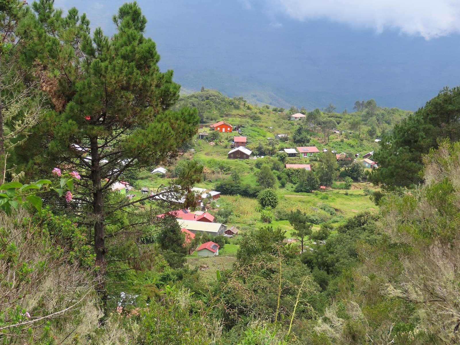 The hamlet of La Nouvelle in the Cirque de Mafate, Réunion, its scattered tin-roofed houses and garden plots spread over a green shelf below the cloud-covered rampart of the cirque