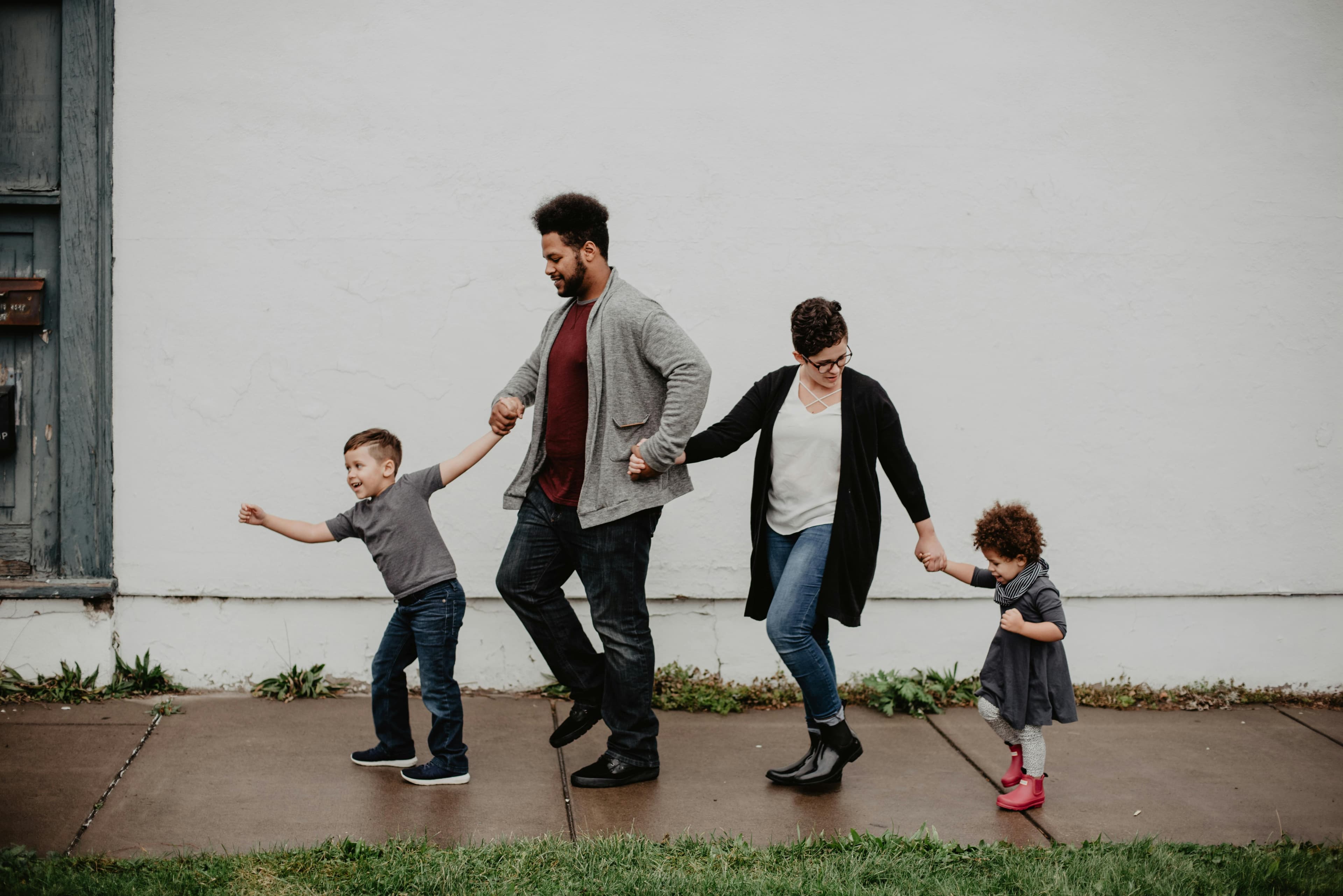 A joyful family of four walks hand in hand along a sidewalk, with the children playfully leading the way. This candid moment captures family togetherness, love, and the simplicity of enjoying time outdoors.