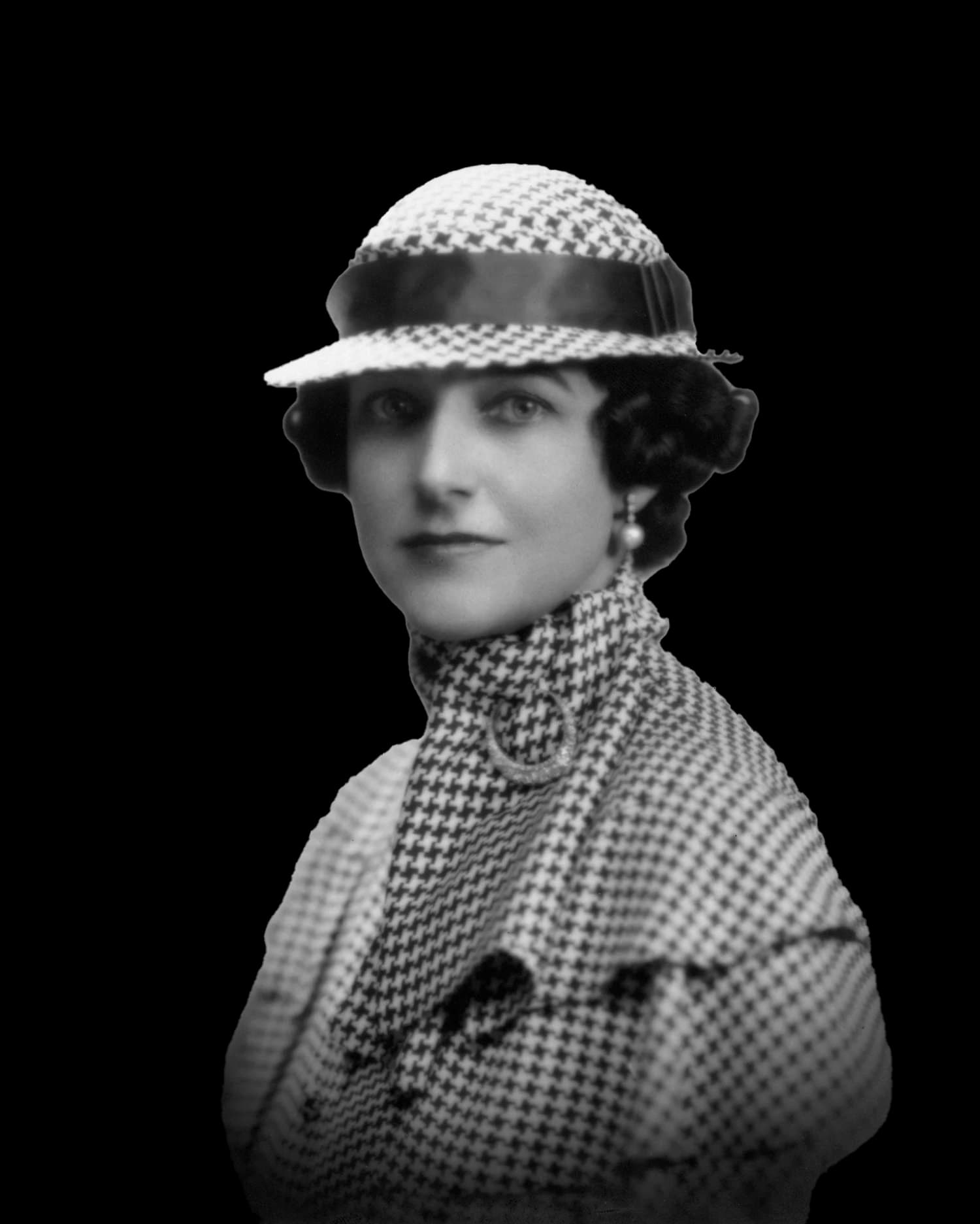 A vintage black-and-white portrait of a woman wearing a stylish houndstooth-patterned outfit, including a matching hat with a glossy band and a high-necked coat. Her hair is styled in classic soft waves, and she accessorizes with pearl earrings, evoking 1930s or 1940s fashion elegance. The image exudes a timeless, sophisticated look, highlighting early 20th-century women's fashion trends.