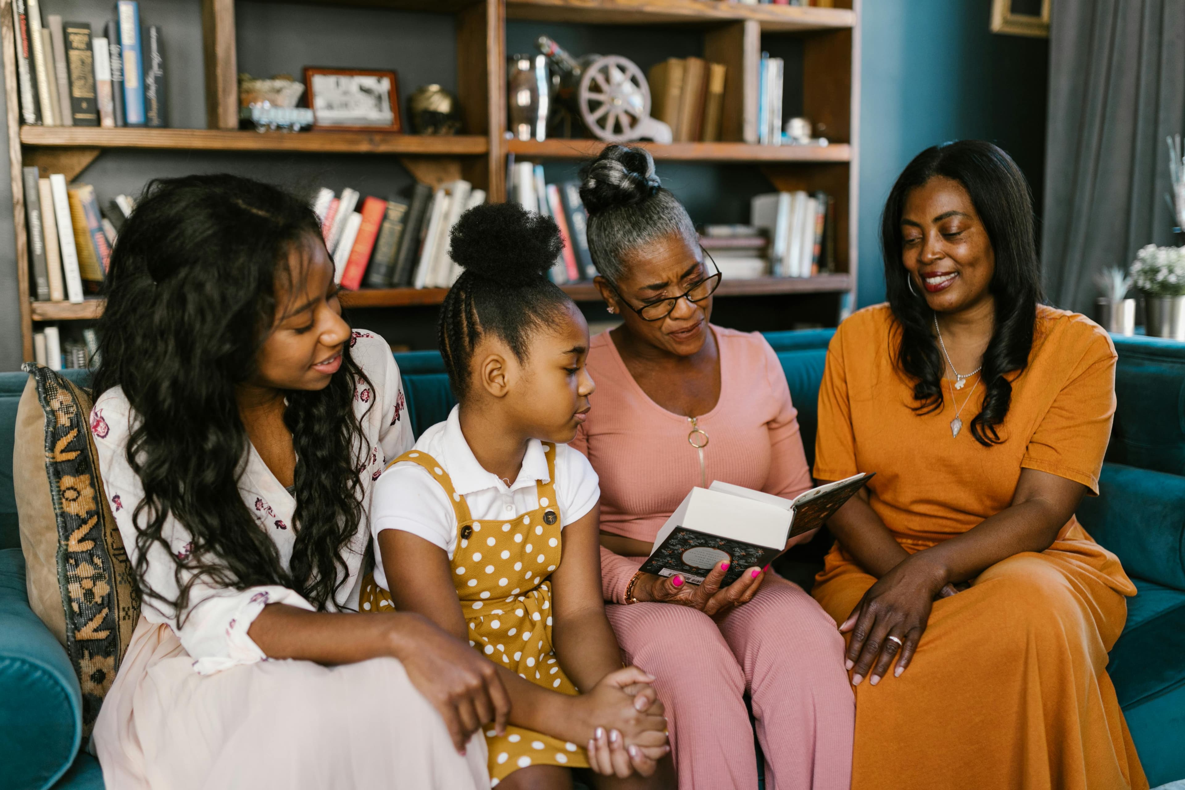 A multigenerational family gathers in a cozy living room, with a grandmother reading a book to her daughter and granddaughters. Surrounded by bookshelves, the scene emphasizes family connection, shared learning, and the joy of storytelling.