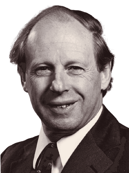 A black-and-white portrait of a middle-aged man with thinning hair and a warm smile, dressed in a suit and patterned tie. The close-up, formal pose highlights his friendly expression and conveys a sense of professionalism and experience, giving the image a classic, respectful tone.