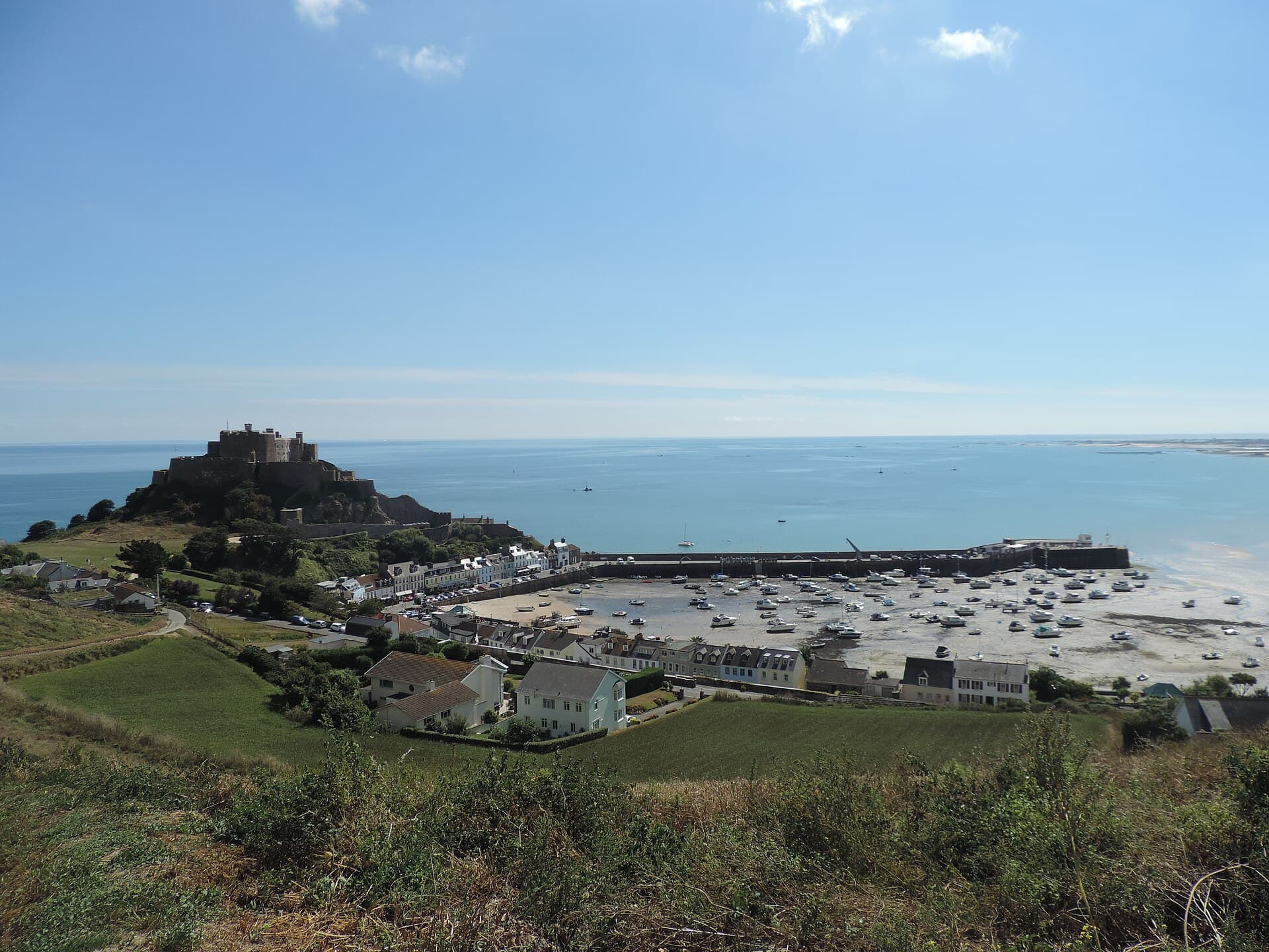 Mont Orgueil castle on its granite headland above the village and harbour of Gorey, Jersey, seen at low tide with boats resting on the sand